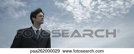 Man in suit standing with sky in background, low angle view View Large Photo Image Stock Photo - Man in suit standing with sky in background, low angle view. Fotosearch