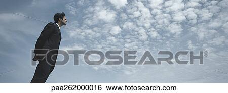 Stock Photograph - Man in suit standing with sky in background, low angle view. Fotosearch