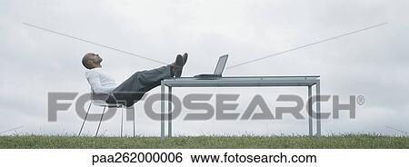 Man sitting in chair outdoors with feet on table and laptop on table, in front of overcast sky View Large Photo Image Stock Photograph - Man sitting in chair outdoors with feet on table and laptop on table, in front of overcast sky. Fotosearch