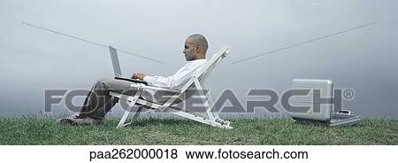 Man sitting in lounge chair with laptop on lap, side view, open metallic briefcase on ground behind him View Large Photo Image Stock Photo - Man sitting in lounge chair with laptop on lap, side view, open metallic briefcase on ground behind him. Fotosearch
