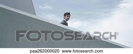 Stock Image - Man standing behind concrete wall, low angle view. Fotosearch