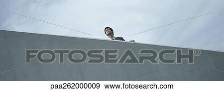 Stock Photo - Man standing behind concrete wall, low angle view. Fotosearch