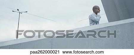 Stock Image - Man standing behind concrete wall talking on cell phone, low angle view. Fotosearch