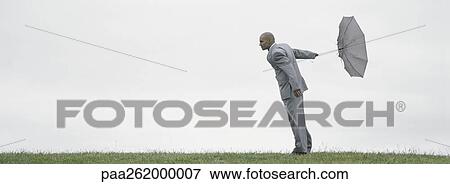 Man standing on grass holding inside-out umbrella behind him View Large Photo Image Stock Photo - Man standing on grass holding inside-out umbrella behind him. Fotosearch