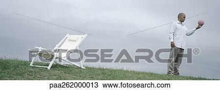 Man standing on grass near lounge chair holding ball in hand View Large Photo Image Stock Image - Man standing on grass near lounge chair holding ball in hand. Fotosearch
