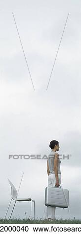 Woman standing on grass holding metallic briefcase in front of chair, sky in background View Large Photo Image Stock Image - Woman standing on grass holding metallic briefcase in front of chair, sky in background. Fotosearch