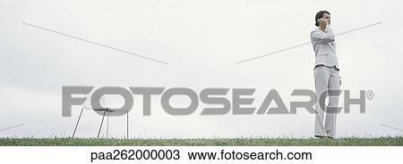 Woman standing outdoors on grass talking on cell phone, with chair, in front of overcast sky View Large Photo Image Stock Image - Woman standing outdoors on grass talking on cell phone, with chair, in front of overcast sky. Fotosearch