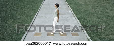 Stock Photo - Woman stepping on wood squares across concrete path, full length. Fotosearch
