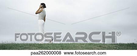 Woman walking on grass talking on cell phone, metallic briefcase on ground behind her View Large Photo Image Stock Photo - Woman walking on grass talking on cell phone, metallic briefcase on ground behind her. Fotosearch
