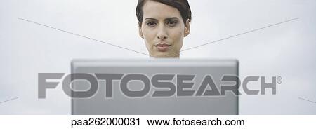 Stock Image - Woman's head seen over edge of computer screen, sky in background. Fotosearch