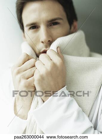 Picture - Man holding sweater around neck, covering part of face. Fotosearch