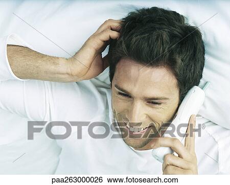Man lying in bed holding cordless phone to ear, smiling View Large Photo Image Stock Photograph - Man lying in bed holding cordless phone to ear, smiling. Fotosearch