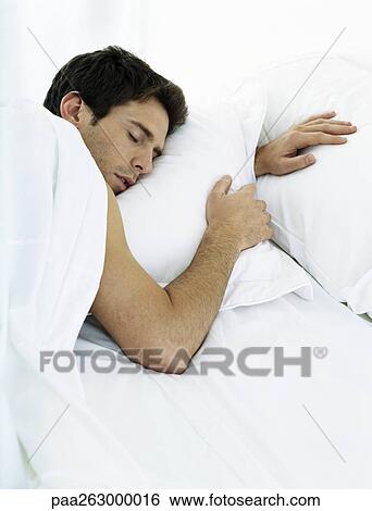 Stock Photograph - Man lying on stomach on bed with eyes closed. Fotosearch