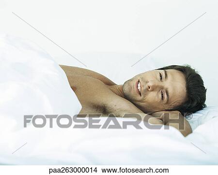 Man lying shirtless on bed looking at camera View Large Photo Image Picture - Man lying shirtless on bed looking at camera. Fotosearch