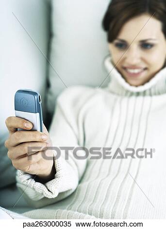 Woman leaning back on pillow holding up cell phone and smiling View Large Photo Image Stock Photography - Woman leaning back on pillow holding up cell phone and smiling. Fotosearch