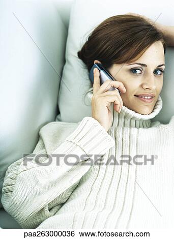 Woman lying back on pillow, holding cell phone to ear, smiling at camera View Large Photo Image Stock Photograph - Woman lying back on pillow, holding cell phone to ear, smiling at camera. Fotosearch