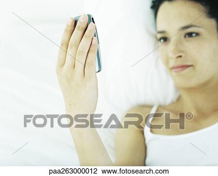 Woman lying on back on bed, looking at cell phone View Large Photo Image Stock Image - Woman lying on back on bed, looking at cell phone. Fotosearch