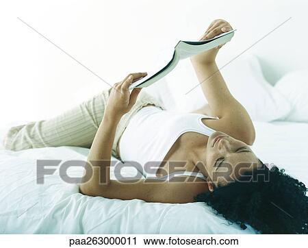 Woman lying on bed holding up magazine, reading View Large Photo Image Stock Image - Woman lying on bed holding up magazine, reading. Fotosearch