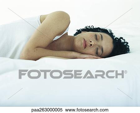 Stock Photography - Woman lying on side on bed with hands under head and eyes closed. Fotosearch