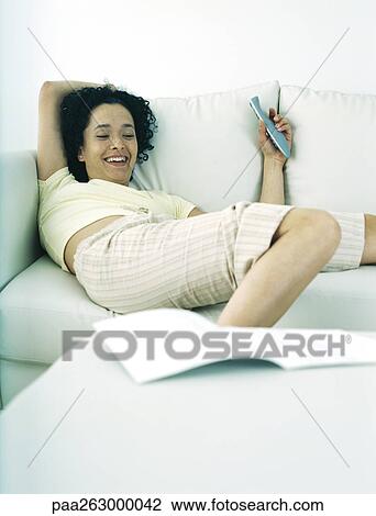 Woman lying on sofa holding remote control, smiling View Large Photo Image Stock Image - Woman lying on sofa holding remote control, smiling. Fotosearch