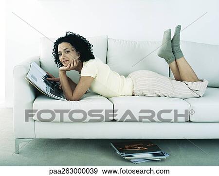 Woman lying on stomach on sofa, holding magazine, head on hand, looking at camera View Large Photo Image Stock Photo - Woman lying on stomach on sofa, holding magazine, head on hand, looking at camera. Fotosearch