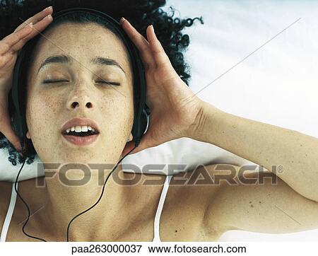 Stock Photo - Woman wearing earphones holding hands to side of head with eyes closed and mouth open. Fotosearch