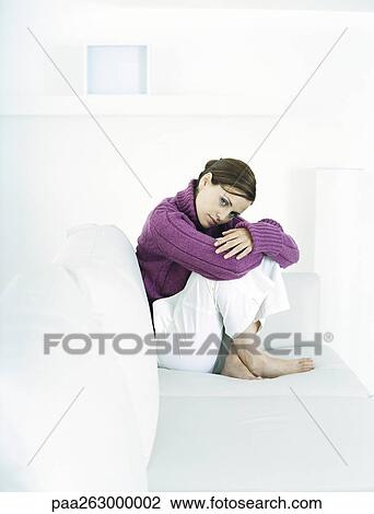 Young woman sitting barefoot on sofa with knees up and head bent forward View Large Photo Image Stock Image - Young woman sitting barefoot on sofa with knees up and head bent forward. Fotosearch