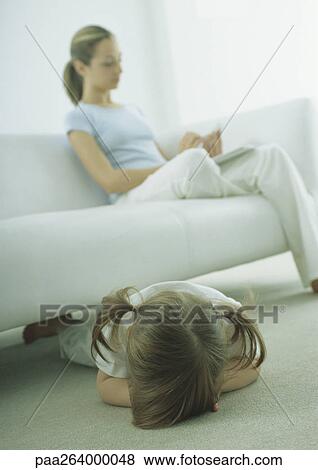 Little girl lying face down on floor, young woman sitting on sofa, reading View Large Photo Image Stock Photo - Little girl lying face down on floor, young woman sitting on sofa, reading. Fotosearch