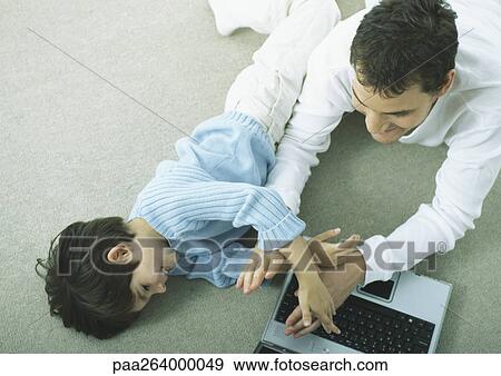 Stock Photo - Man and little boy lying on floor with laptop playing. Fotosearch