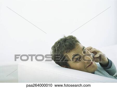 Man sitting on sofa, looking back over shoulder, holding cell phone to ear View Large Photo Image Stock Image - Man sitting on sofa, looking back over shoulder, holding cell phone to ear. Fotosearch