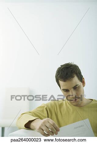 Stock Image - Man sitting on sofa looking down at document. Fotosearch