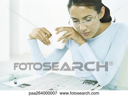 Stock Photo - Woman holding mug looking down at newspaper. Fotosearch