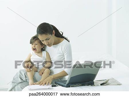 Woman sitting on bed with little girl on lap crying, looking down at paper View Large Photo Image Stock Photo - Woman sitting on bed with little girl on lap crying, looking down at paper. Fotosearch