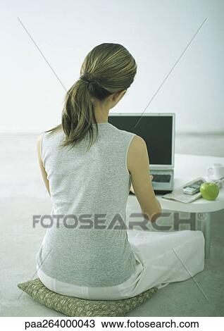 Woman sitting on cushion on floor at coffee table with laptop, rear view View Large Photo Image Stock Image - Woman sitting on cushion on floor at coffee table with laptop, rear view. Fotosearch