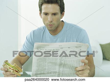 Young man reading newspaper and eating sandwich View Large Photo Image Stock Image - Young man reading newspaper and eating sandwich. Fotosearch
