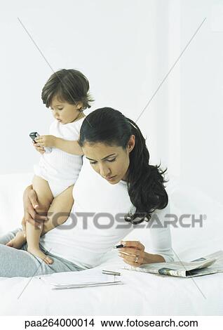Picture - Young woman propped up on elbow holding pen with one hand, holding little girl with other arm. Fotosearch