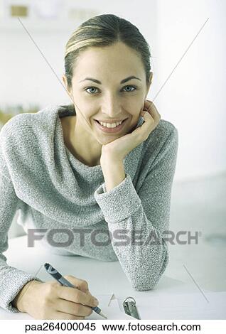 Young woman sitting at table, leaning on elbow, smiling View Large Photo Image Stock Photography - Young woman sitting at table, leaning on elbow, smiling. Fotosearch