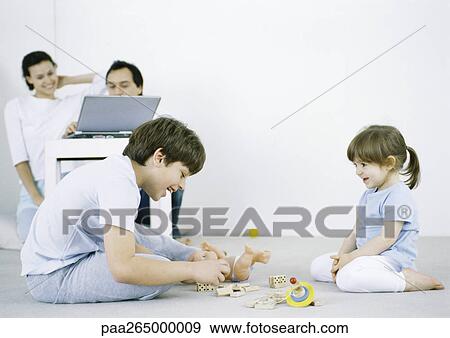 Boy and girl sitting on floor playing, man and woman using laptop in background View Large Photo Image Stock Photo - Boy and girl sitting on floor playing, man and woman using laptop in background. Fotosearch