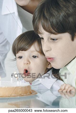 Stock Image - Boy and little girl blowing out candles on cake, mother in background. Fotosearch