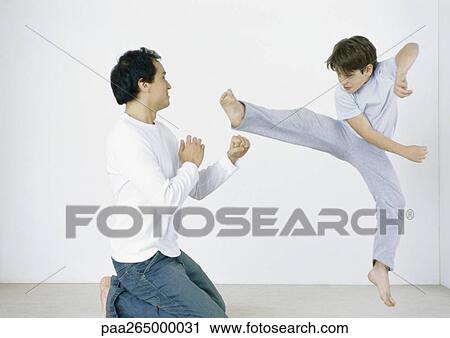 Stock Image - Boy giving karate kick in mid air, man on knees with fists out. Fotosearch