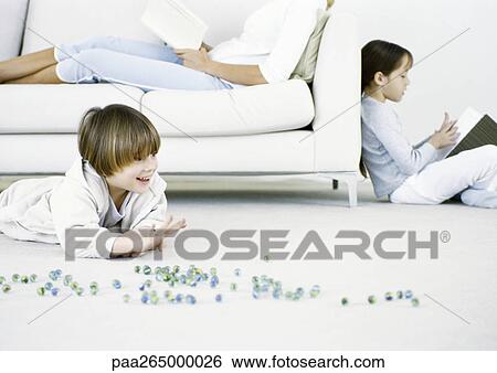 Boy playing marbles on floor, woman and girl reading in background View Large Photo Image Stock Photograph - Boy playing marbles on floor, woman and girl reading in background. Fotosearch