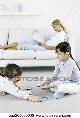 Girl and boy playing cards on floor, woman sitting on sofa reading in background View Large Photo Image Stock Photography - Girl and boy playing cards on floor, woman sitting on sofa reading in background. Fotosearch