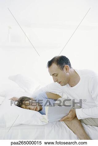 Man sitting on edge of bed reading book to girl lying in bed View Large Photo Image Stock Photography - Man sitting on edge of bed reading book to girl lying in bed. Fotosearch