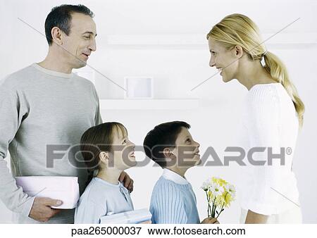 Stock Photo - Man with boy and girl facing woman with gifts and flowers. Fotosearch
