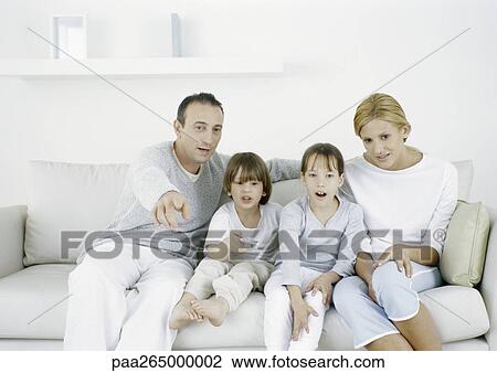 Stock Image - Parents with sitting on sofa with daughter and son, father pointing straight ahead. Fotosearch