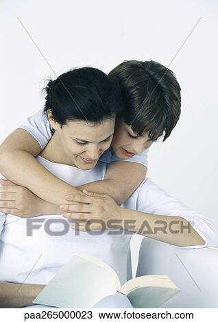 Woman and son reading book, boy with arms around woman, looking over her shoulder View Large Photo Image Stock Image - Woman and son reading book, boy with arms around woman, looking over her shoulder. Fotosearch