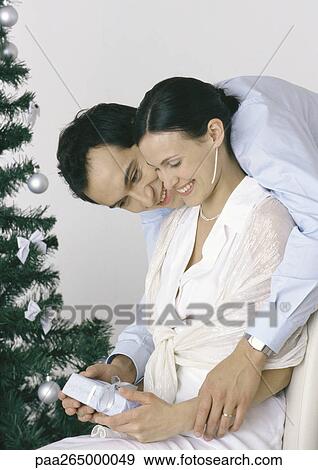 Woman holding gift, man bending over her shoulder, Christmas tree in background View Large Photo Image Stock Photo - Woman holding gift, man bending over her shoulder, Christmas tree in background. Fotosearch
