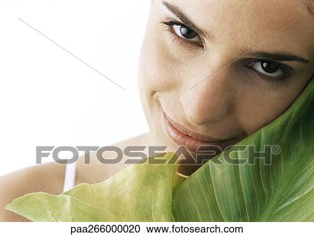 Woman tilting head against green leaf, smiling at camera, close-up View Large Photo Image Stock Image - Woman tilting head against green leaf, smiling at camera, close-up. Fotosearch