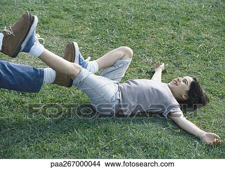 Picture - Boy lying on back on grass with feet pushing against man's feet. Fotosearch