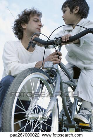 Boy on bicycle looking at father holding onto bicycle, low angle view View Large Photo Image Stock Image - Boy on bicycle looking at father holding onto bicycle, low angle view. Fotosearch